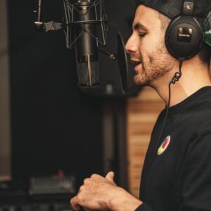 A man wearing headphones and recording vocals in a music studio with a microphone.